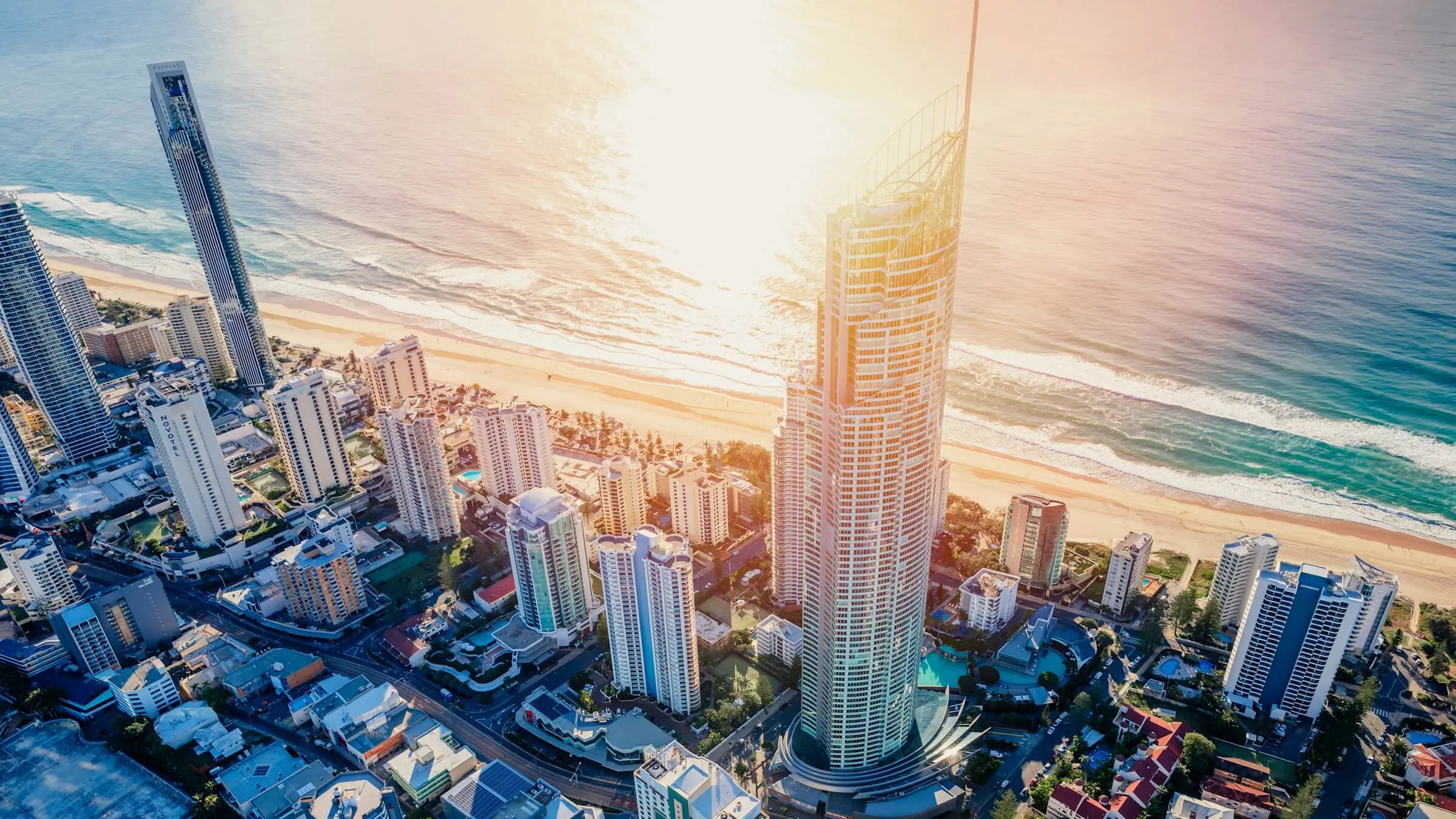 Aerial view of the Q1 tower and its spire rising over the Surfers Paradise high-rises, with the beach and ocean lit by the morning sun